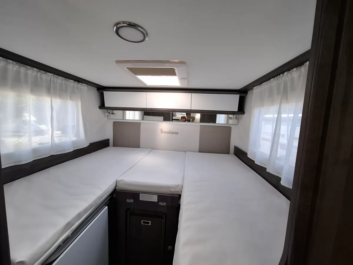 Dormitorio trasero de la autocaravana perfilada con camas, ventanas y armarios altos