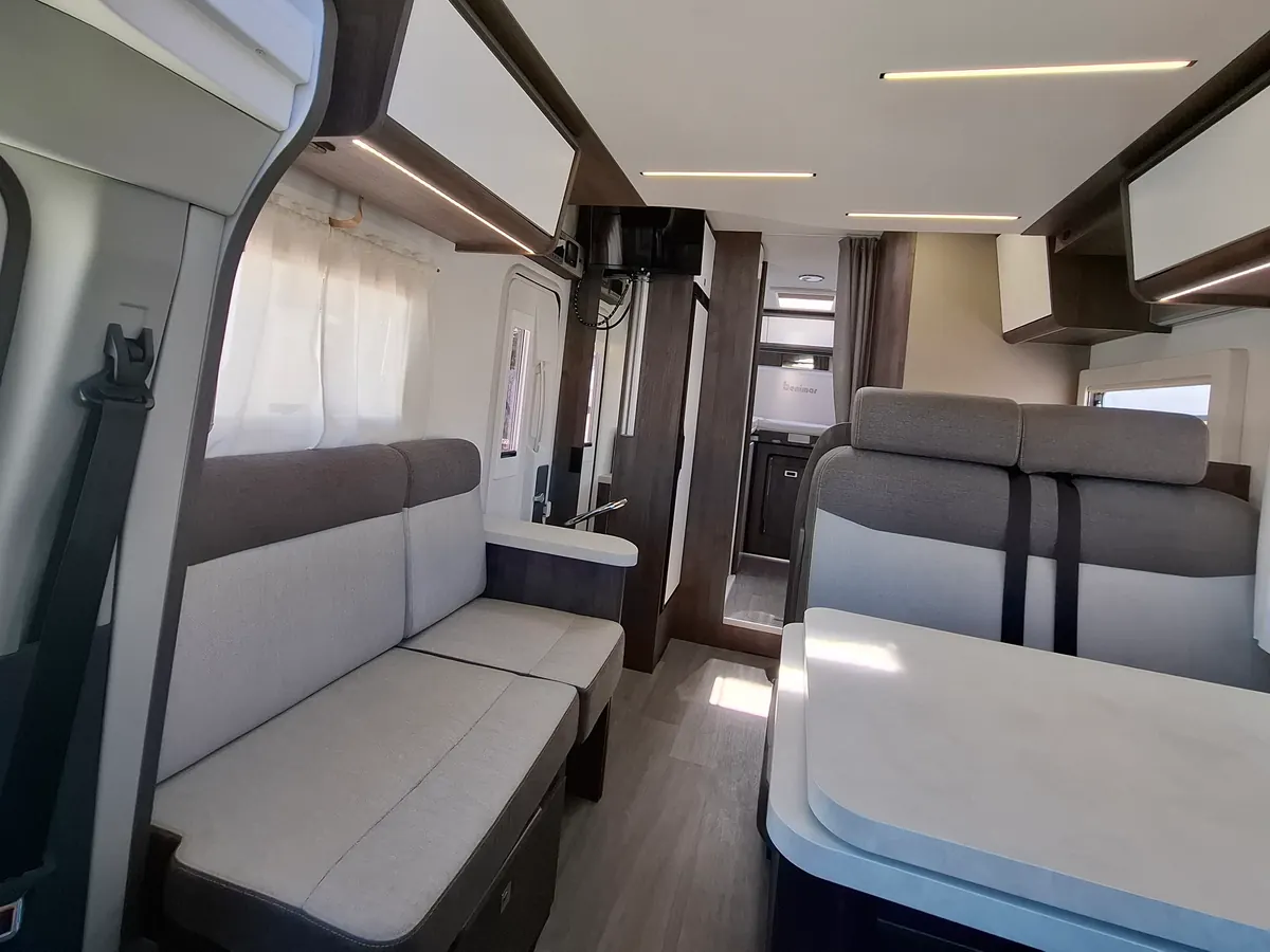 Interior de la autocaravana perfilada de Camperaventura: salón con sofá, mesa y pasillo hacia el baño y el dormitorio