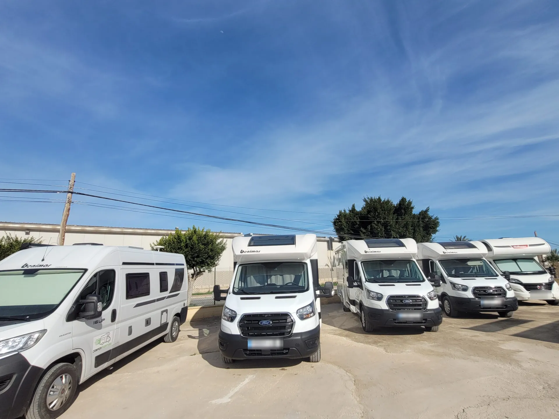 Flota de autocaravanas perfiladas y furgonetas camper blancas de Camperaventura aparcadas en fila bajo un cielo azul