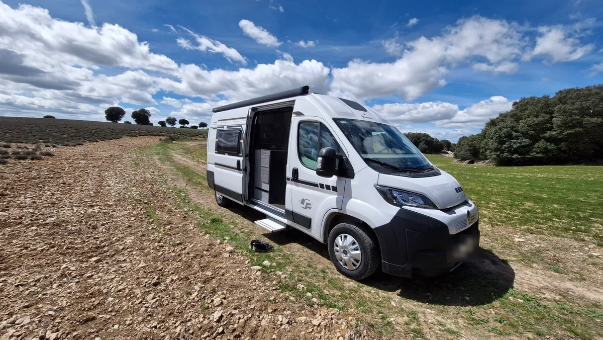 Furgoneta camper de alquiler de Camperaventura con la puerta lateral abierta, aparcada en el campo